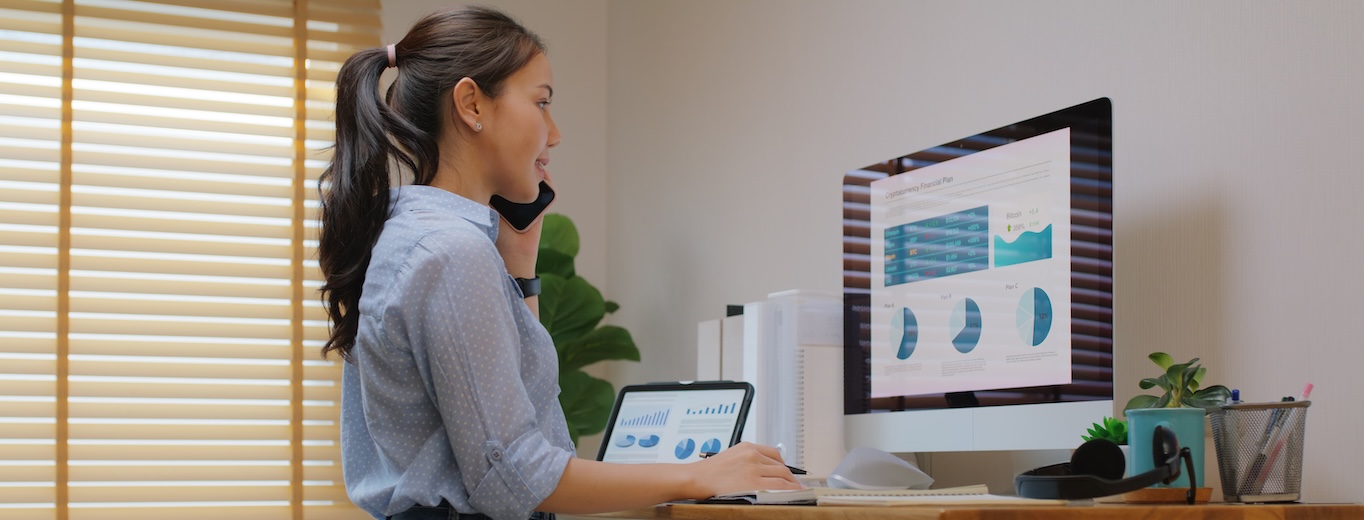 Arbeitsplatz Ergonomie Frau arbeitet im ergonomischen Homeoffice an Computer und Tablet, spricht am Telefon, mit aufgeräumtem Schreibtisch, Tageslicht und Pflanzen für gesunde Arbeitsplatz Ergonomie.